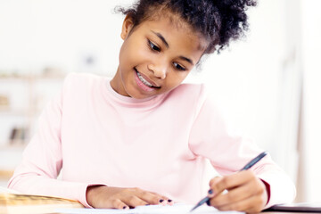 African Teen Girl Doing Homework Writing In Exercise-Book Sitting At Desk At Home. Selective Focus