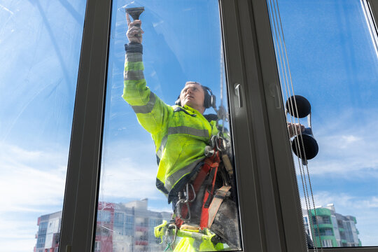 Professional Window Cleaner Performing His Job on High Rise Building, Capturing the Dedication and Safety Measures in His Day-to-Day Work Environment and Routine.