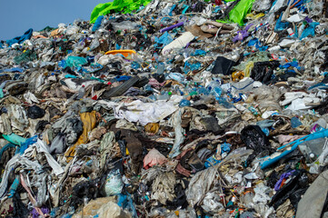 A large accumulation of plastic waste and organic material is visible at a landfill site, highlighting environmental concerns