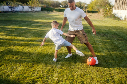 Playful father and little son in action playing soccer together in backyard.