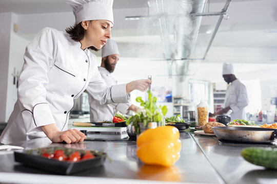 Dedicated chef testing the flavors of a gourmet dish at the kitchen counter, adjusting the seasoning for the perfect taste. Woman focusing on fresh ingredients for fine dining presentation. - Powered by Adobe
