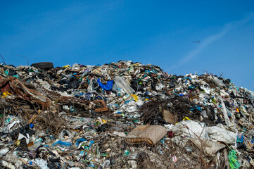 A vast landfill overflowing with plastic, fabric, and other debris under a bright blue sky...