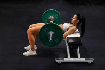 Side view of strong muscular sportswoman doing hip thrusts with barbell at gym.
