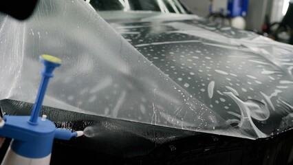 Professional car detailer applying paint protection film on vehicle hood