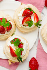 Meringue nests mini pavlovas with whipped cream and strawberries on a plate.top veiw