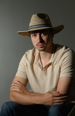 Young man in a straw hat seated against a softly lit backdrop, showcasing a thoughtful expression...