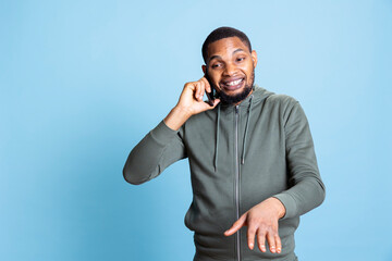Fototapeta premium African american person chatting on his phone call with friends, gossiping and enjoying his leisure time against blue background. Casual relaxed guy being pleased with his conversation.
