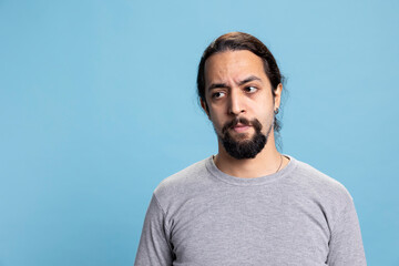 Fototapeta premium Male person standing against blue background with confidence, advertising a vibrant cool attitude in studio. Young adult with curly long hair and beard posing with arms crossed on camera.