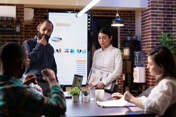 Business team reviews marketing strategies using digital charts on LED screen. Diverse colleagues leverage modern technology for financial analysis and online data insights during late night meeting.