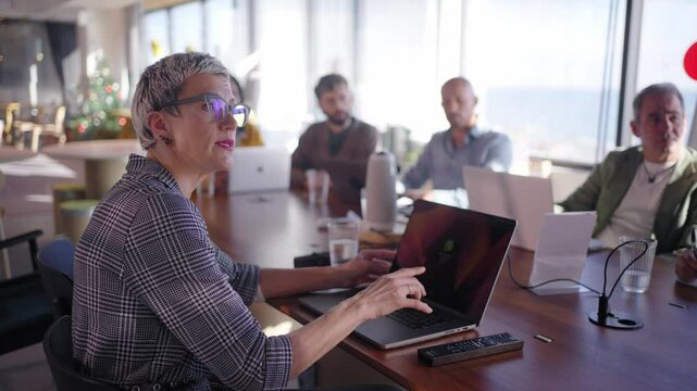 Business woman leading strategic presentation, using laptop while collaborating with team in modern office, fostering dynamic workplace discussion professional interaction. Empowered female leadership