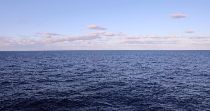 4k Video captured from deck of cruise ship overlooking a vast calm deep blue wide open ocean with light fluffy clouds