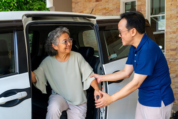 Asian man caregiver or taxi driver helping senior woman patient get in car to get to medical appointments or healthcare therapy sessions at hospital. Assisted elderly patient transportation services.