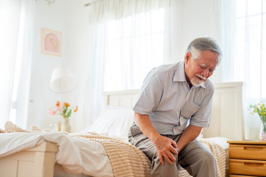 Asian senior mature woman sit on the bed suffering from knee and leg pain. Unhappy elderly feeling pain in joint and tendon from rheumatoid arthritis, osteoarthritis and peripheral neuropathy. - Powered by Adobe