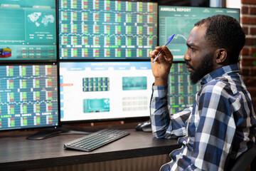 Male investor with a focused look, working at desk, analyzing forex and stock market trends on...