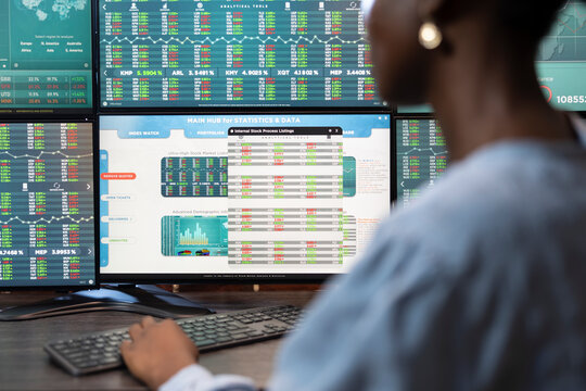 Closeup of black female employee typing on a keyboard at office desk, reviewing stock exchange progress on multiple screens. Selective focus on digital monitor displaying trading statistics and data.