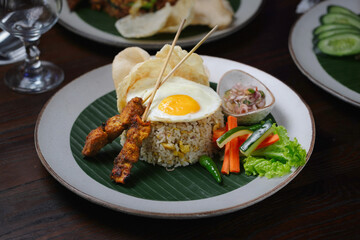 Indonesian Fried Rice with Satay, Fried Egg, and Fresh Vegetables on Banana Leaf