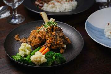 Braised and Grilled Lamb Shank with Delicious Spices and Steamed Vegetables on a Black Plate