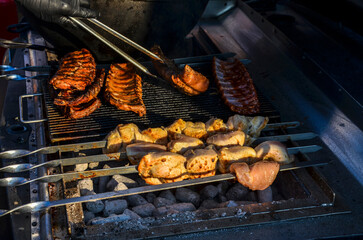 Selection of meats, including kebabs and ribs, are being grilled on a barbecue during a warm evening, showcasing a tasty barbecue dish preparation