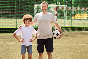 Sports Concept. Portrait of smiling man holding soccer ball and standing with boy on playground,...