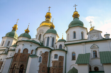 Exterior of Saint Sophia's Cathedral in Kyiv, Ukraine, under a clear blue sky. The cathedral features white walls, green roofs, and golden domes with crosses