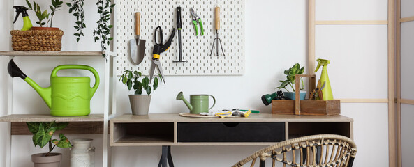 Workplace with gardening tools and plants near white wall
