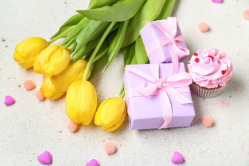 Presents, yellow tulips and tasty cupcake on light background