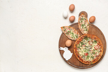 Board with tasty pizza with Easter bunny ears and eggs on white background