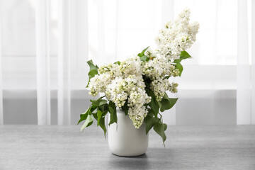 Vase with lilac branches on table near window in room