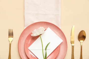 Stylish table setting with beautiful flower and envelope on beige background