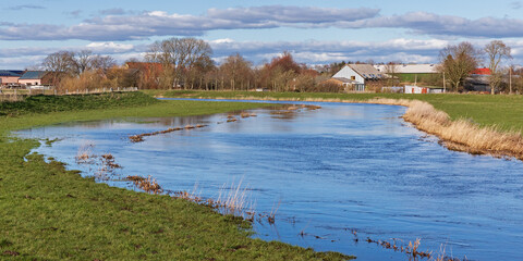 Die bei Frühjahrshochwasser über die Ufer getretene Treene bei Hollingstedt in Schleswig-Holstein, Deutschland. Mit landwirtschaftlichen Gebäuden im Hintergrund.