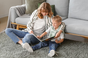 Happy mother and her little son reading book on floor in living room at home