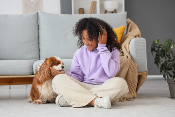 Teen African-American girl in headphones feeding cute cavalier King Charles spaniel at home