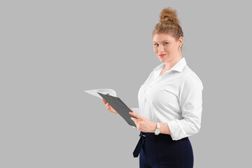 Young beautiful businesswoman in formal clothes with clipboard on grey background