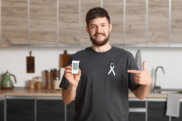 Diabetic young man with blue awareness ribbon and glucometer in kitchen