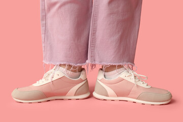 Legs of young woman in stylish sneakers on pink background