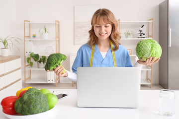Female nutritionist with broccoli and cabbage video chatting at table in office
