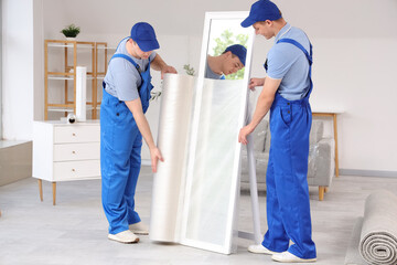 Loaders covering mirror with polyethylene film in stylish room
