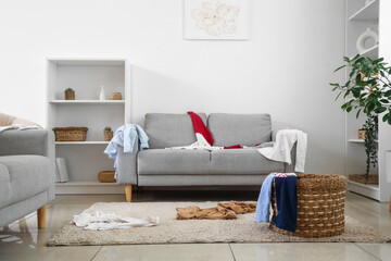 Interior of living room with laundry basket and dirty clothes on sofa