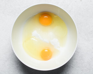Overhead view of egg and sugar in a bowl on a marble countertop, process of making a cake