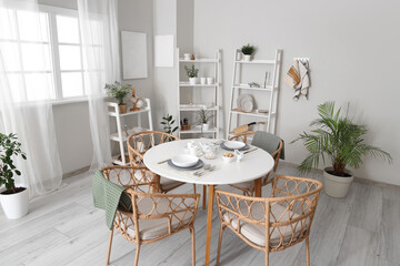 Served dining table with wicker chairs and shelving units in interior of stylish kitchen