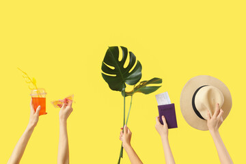 Female hands with cocktail, sunglasses, hat, monstera leaf and passport with tickets on yellow background. Travel concept