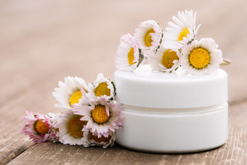 Close up of collagen cream in glass jar with daisies on wooden surface. Skin and body care beauty products. Mockup. Cosmetic packaging, creme moisturiser
