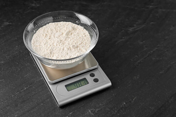 Electronic kitchen scale with bowl of flour on dark textured table. Space for text