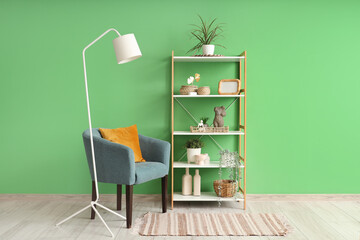 Interior of modern room with comfortable armchair, shelving unit and lamp near green wall