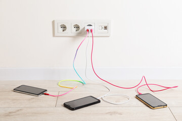 USB adapter with cables plugged into electric socket charging different devices indoors