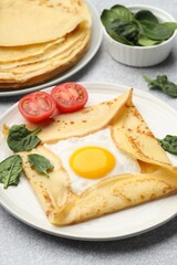 Delicious crepes with egg, tomato and basil on light grey table, closeup