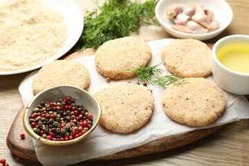 Many uncooked patties and spices on wooden table, closeup