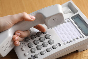 Woman dialing number on telephone at wooden table, closeup