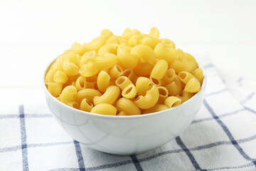 Raw horns pasta in bowl on white table, closeup