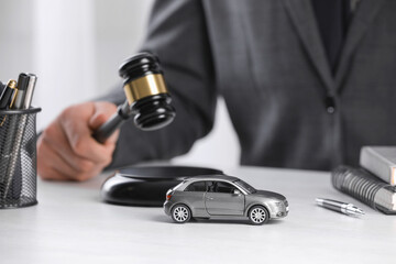 Auto accident law. Man striking gavel at table indoors, focus on toy car